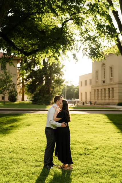 A kiss on the lawn with the sun setting behind the campus