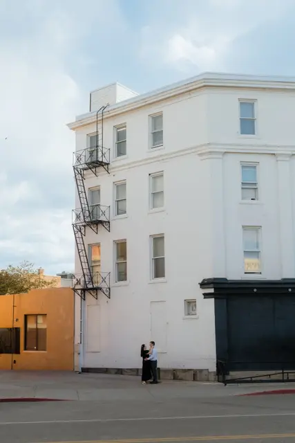 Standing small against a tall white building on a quiet corner