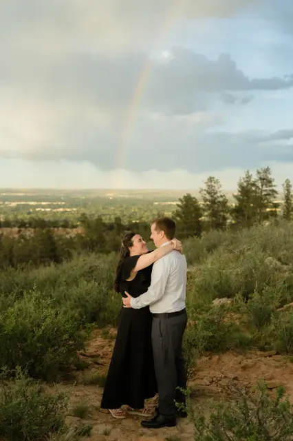 Holding each other on the hillside as a rainbow arcs over the valley