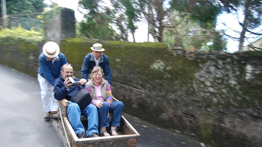 Two passengers riding a wicker toboggan down a street in Monte, Madeira